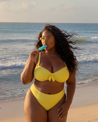 Lemon Drop plus size yellow bikini with high waisted bottoms worn on beach with popsicle at sunset
