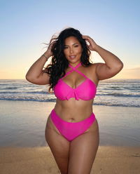 Plus size model wearing Poppin Pink hot pink bikini posing on the beach at sunset with ocean waves behind