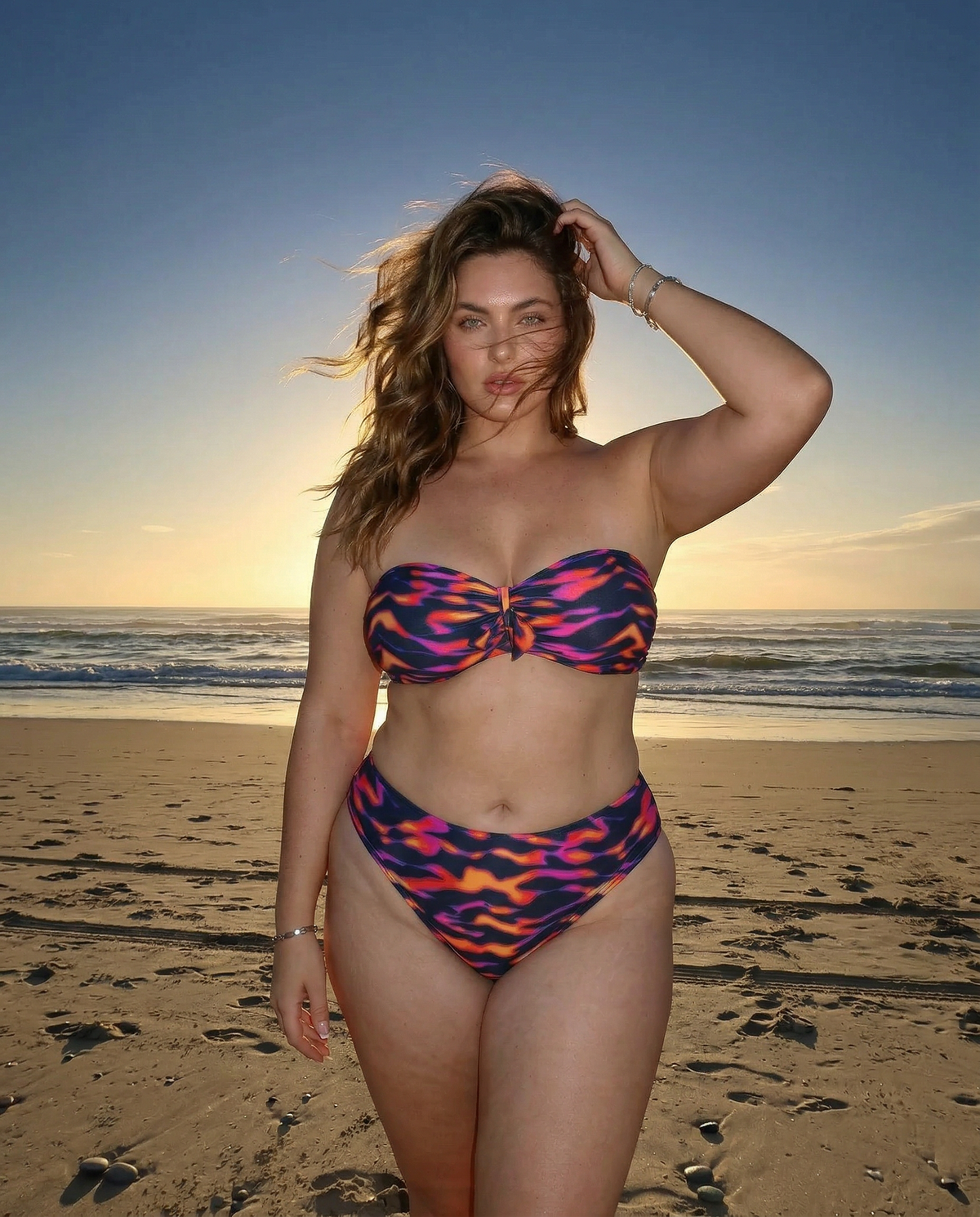 Plus size model wearing Purple Blaze flame print bandeau bikini standing on the beach at sunset with ocean waves behind