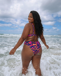Plus size model wearing Purple Blaze flame print bikini walking in ocean waves with back view at the beach
