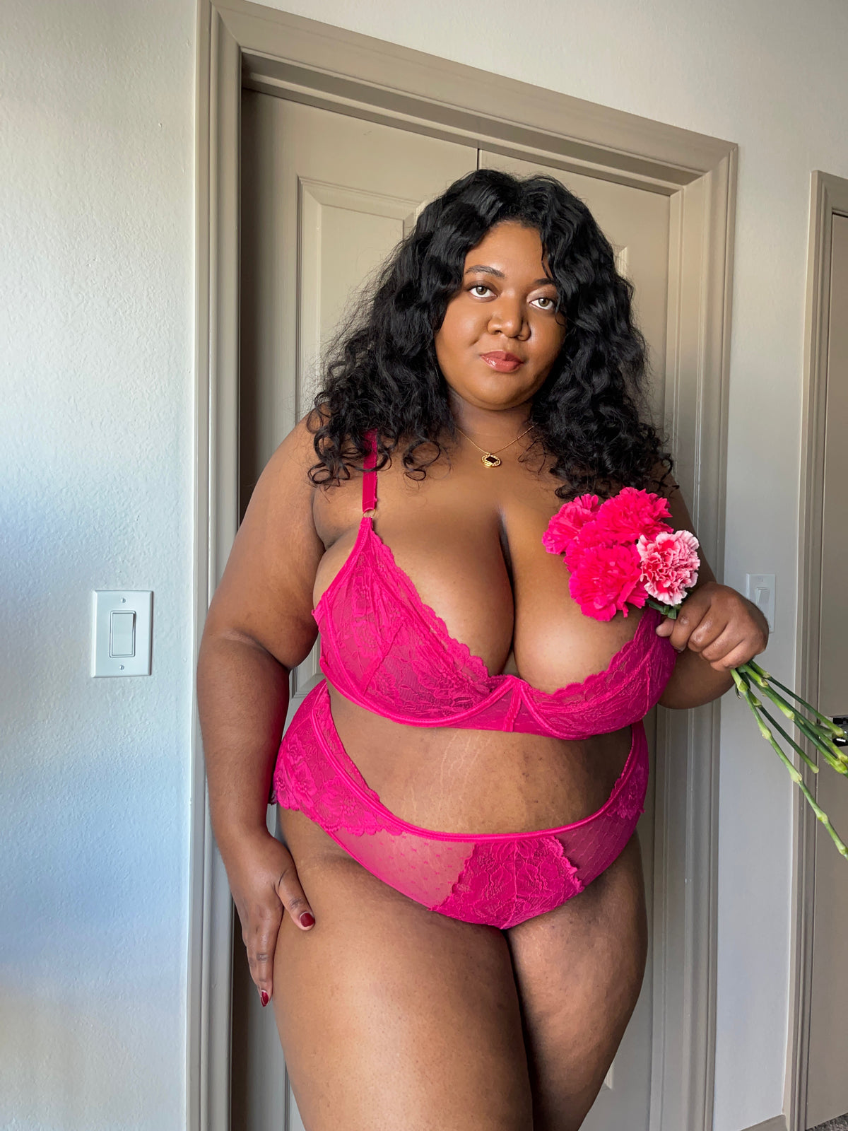 Plus size woman wearing pink lace lingerie set holding flowers in soft natural lighting